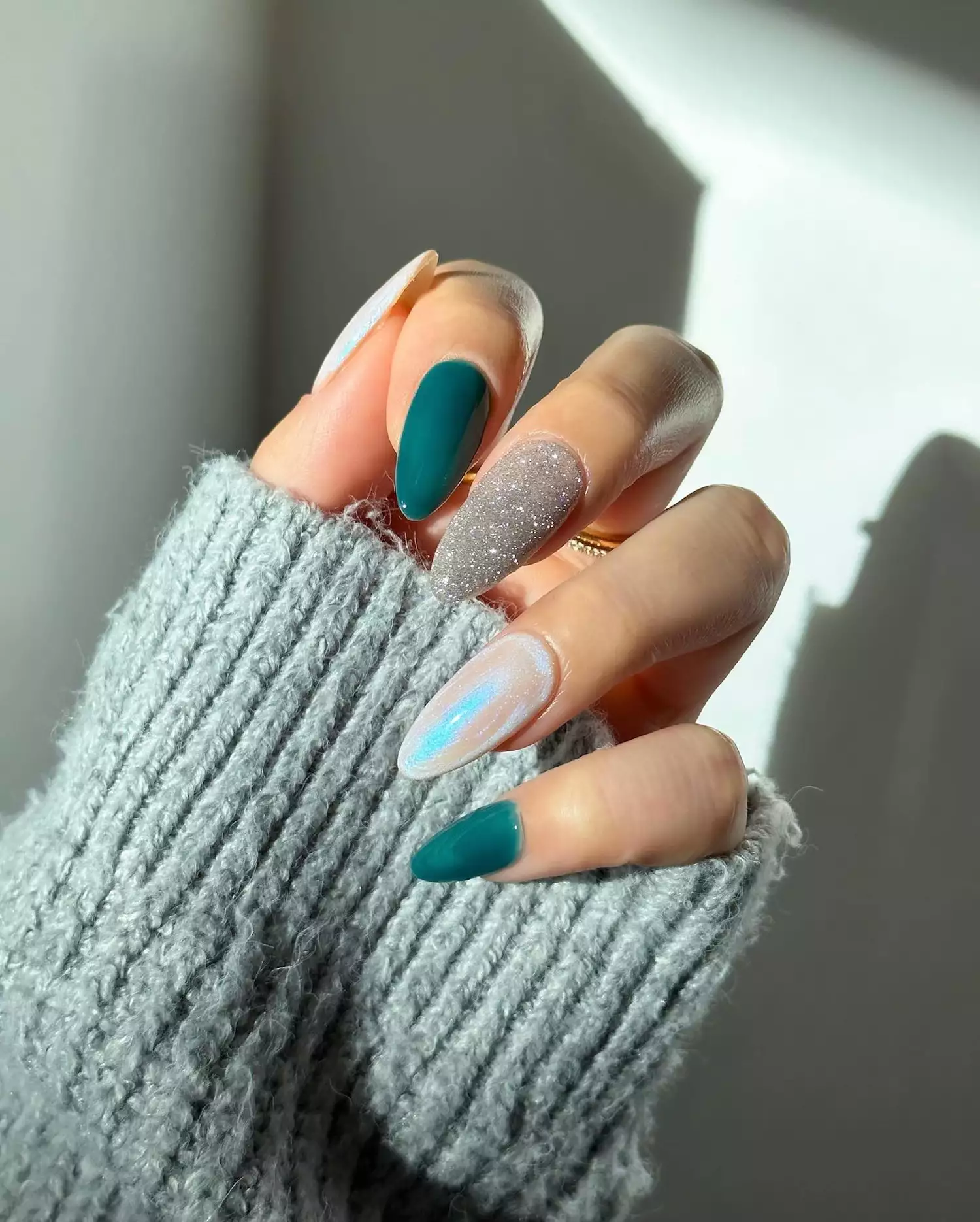 A manicure with teal, silver glitter, and chrome nails