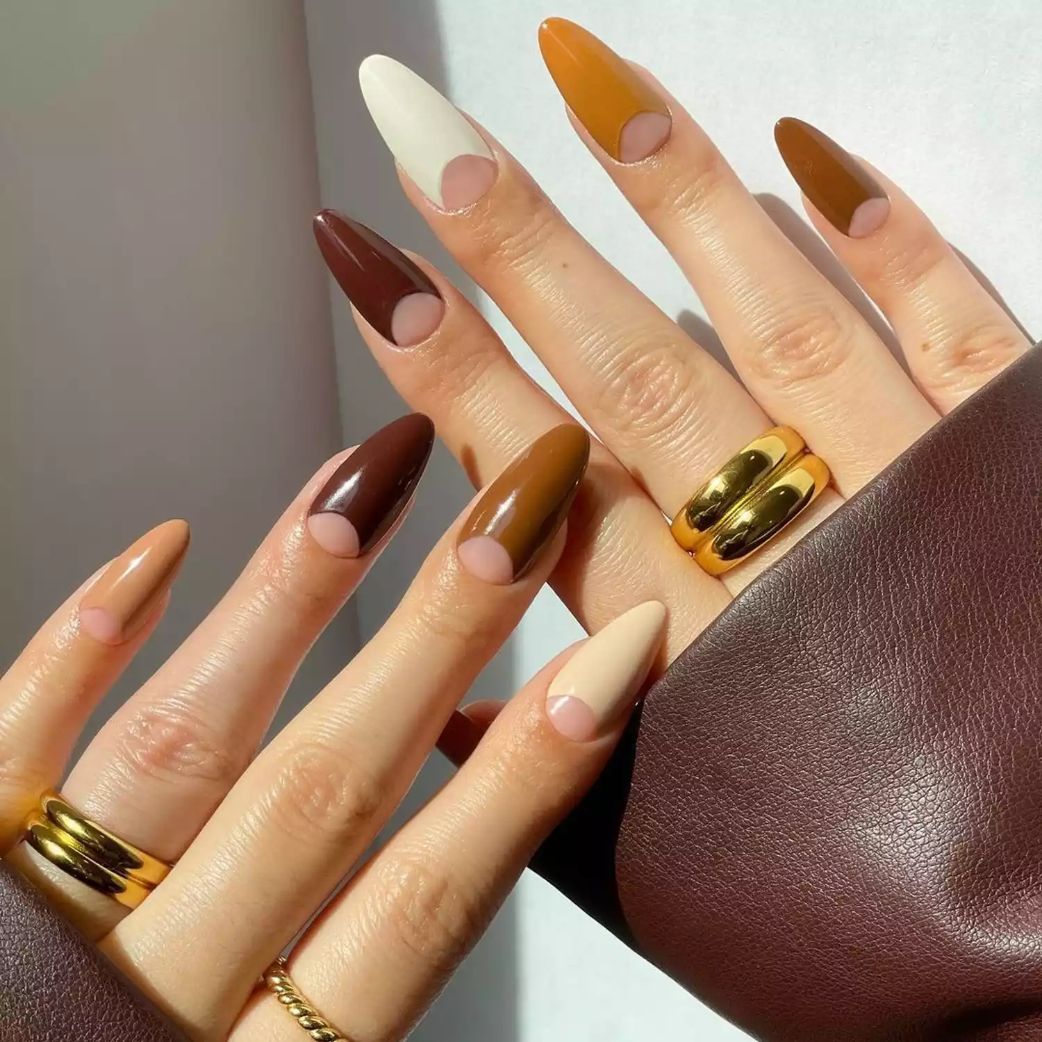 Mocha, caramel, and white chocolate nails with negative-space half moons at the base