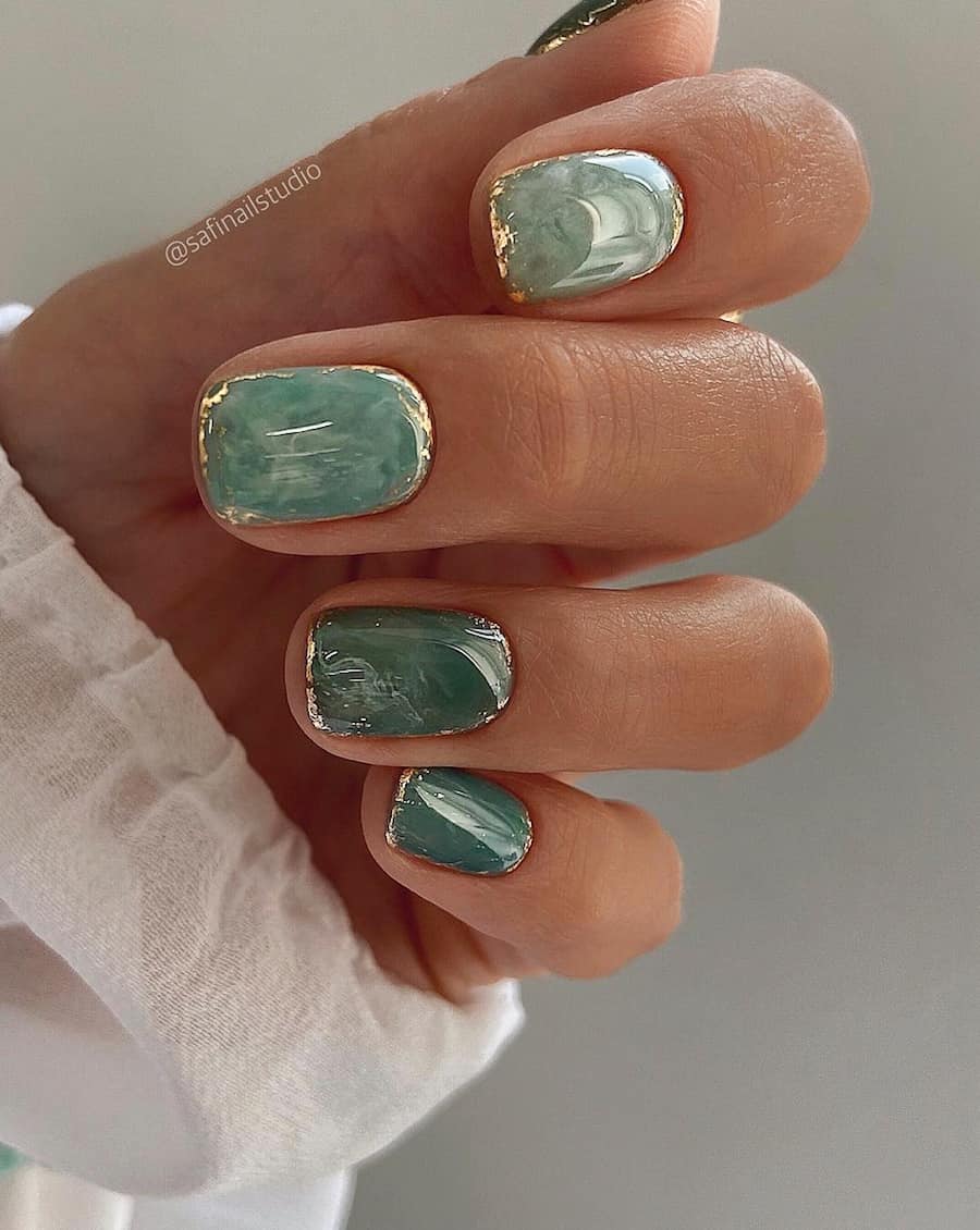 hand with short sage green marble nail designs with gold accents