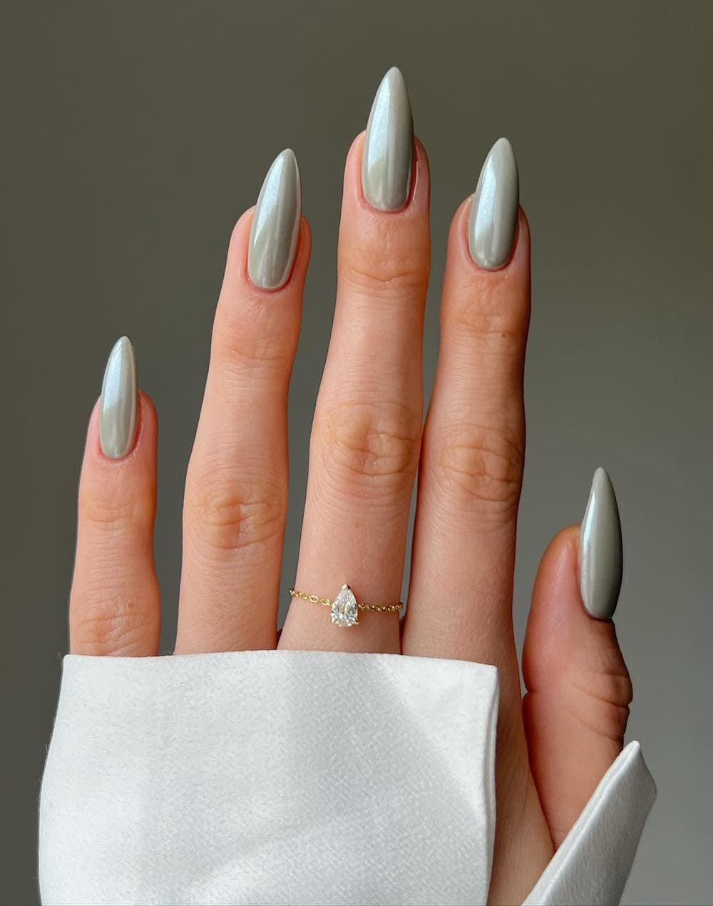 image of a hand with long almond-shaped chrome sage green nails