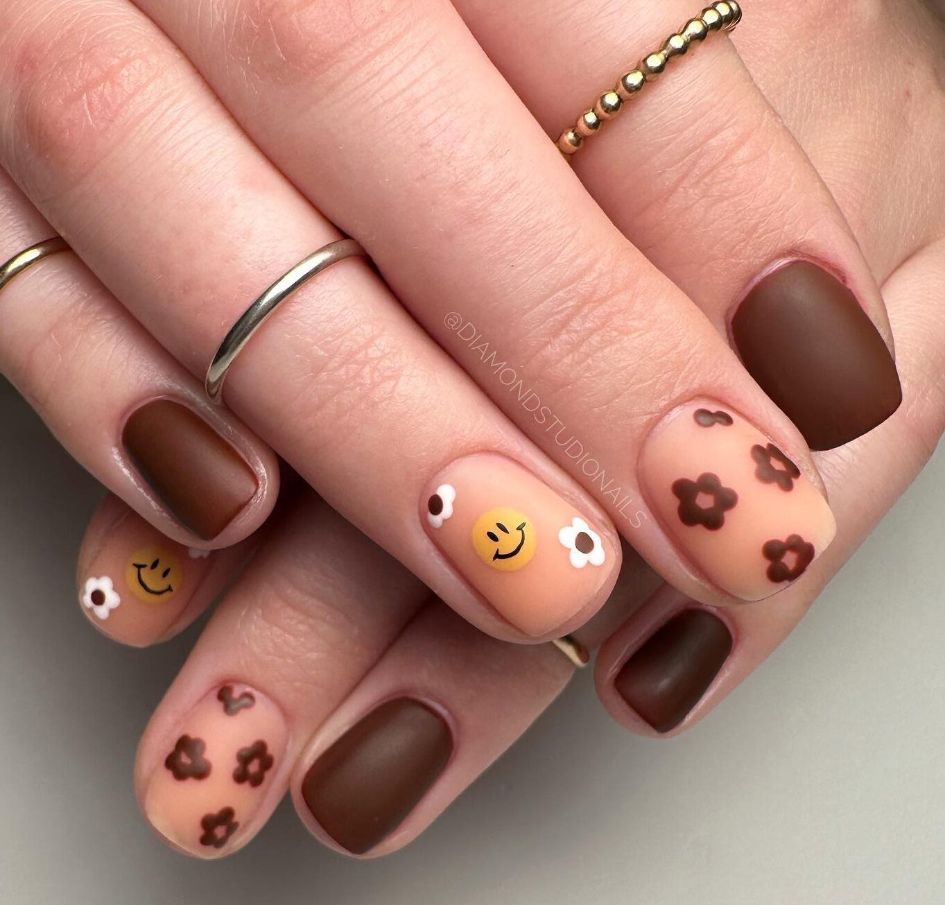 Brown nail polish in matte finish with smileys and brown flowers on short square nails