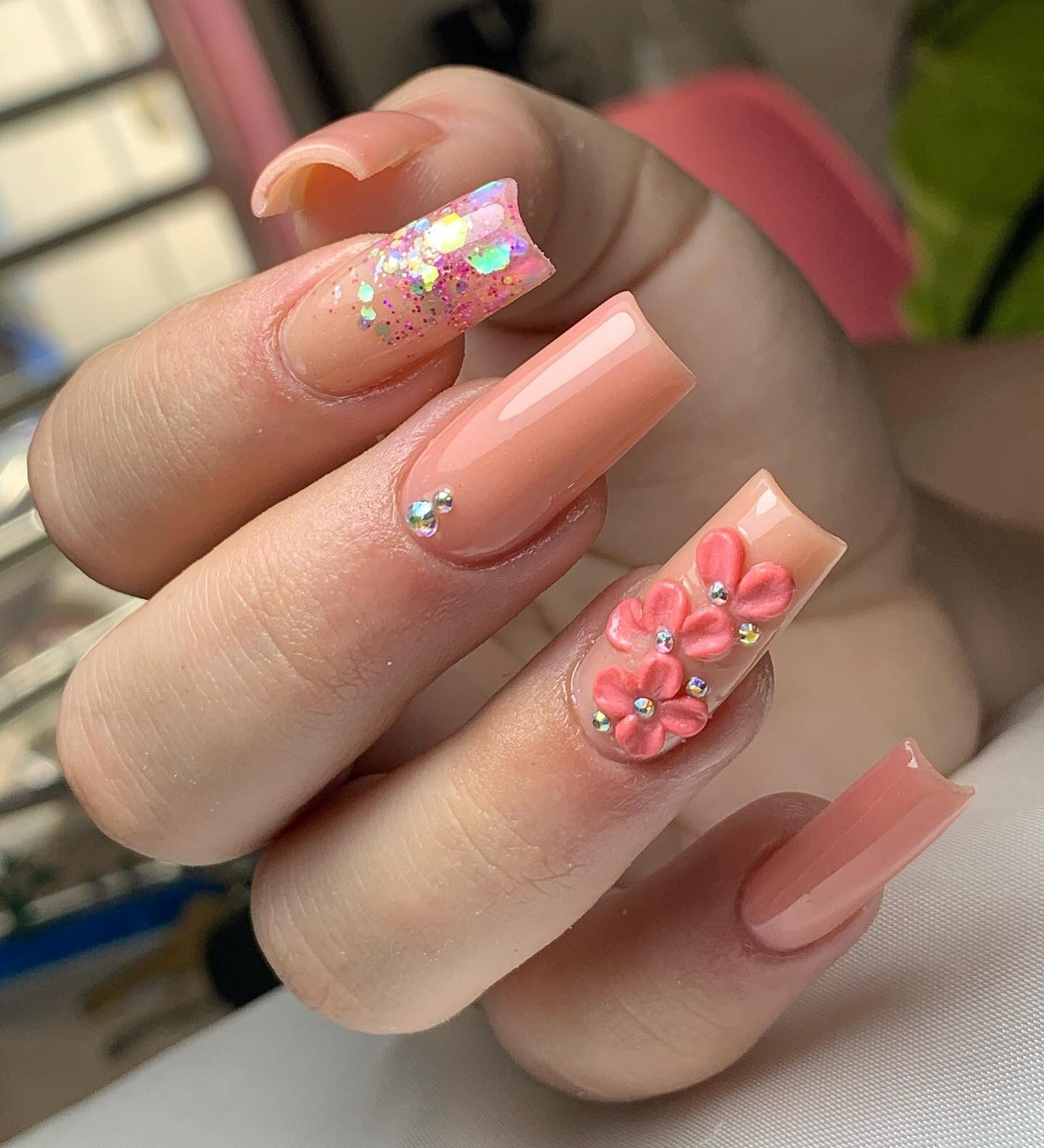 Pale peach nail polish with 3D flowers, stones, and glitters on long square nails