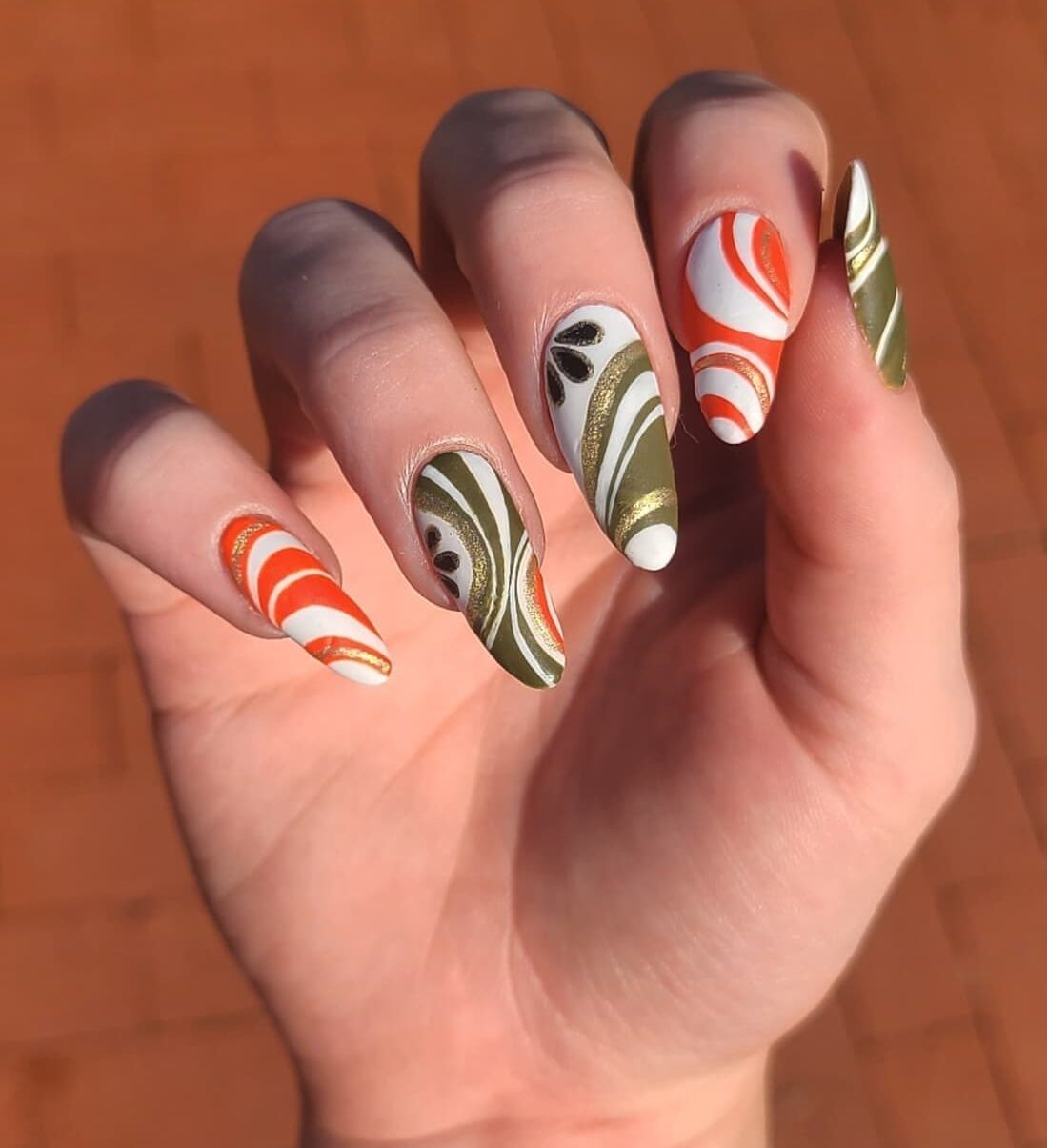 White nail polish with green and orange swirls and glitters on long almond nails