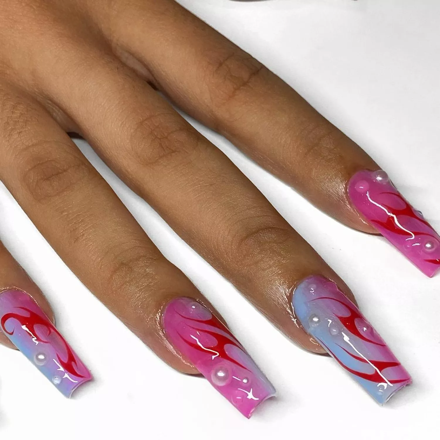 Hand with long pink and blue ombre nails with red designs and pearl accents