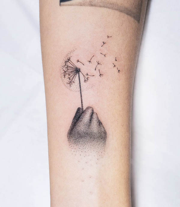 Hand holding a dandelion tattoo by @oitattooer