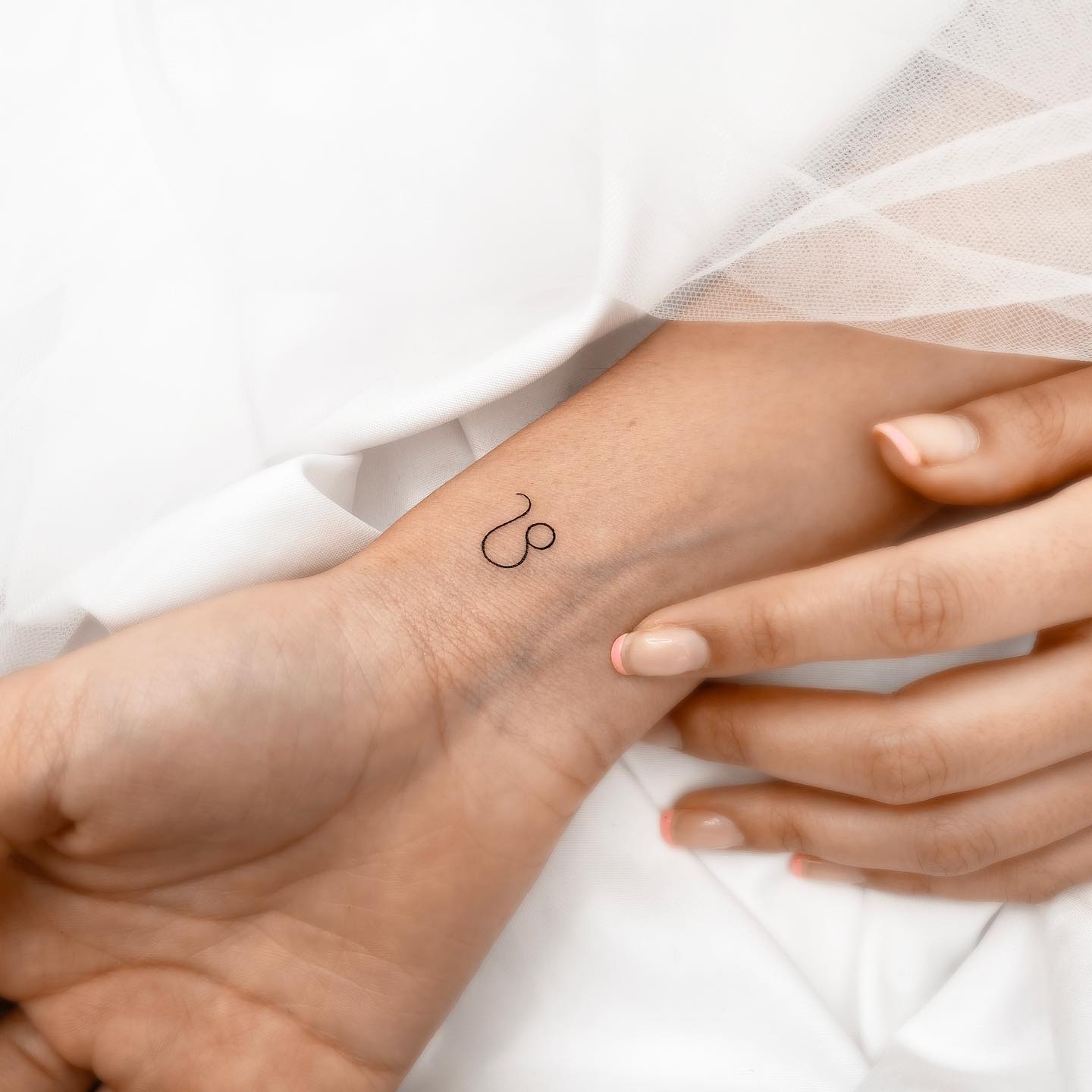 Fine line Leo zodiac symbol tattooed on the wrist, minimalistic style