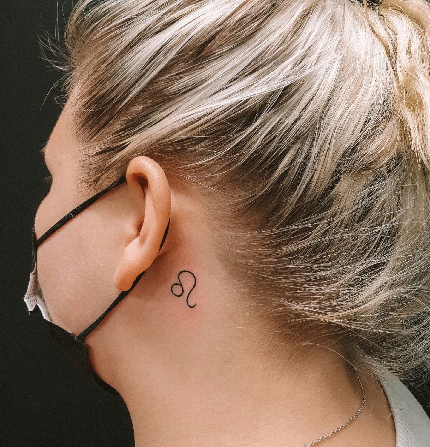 Leo zodiac symbol tattooed behind the ear, minimalistic style