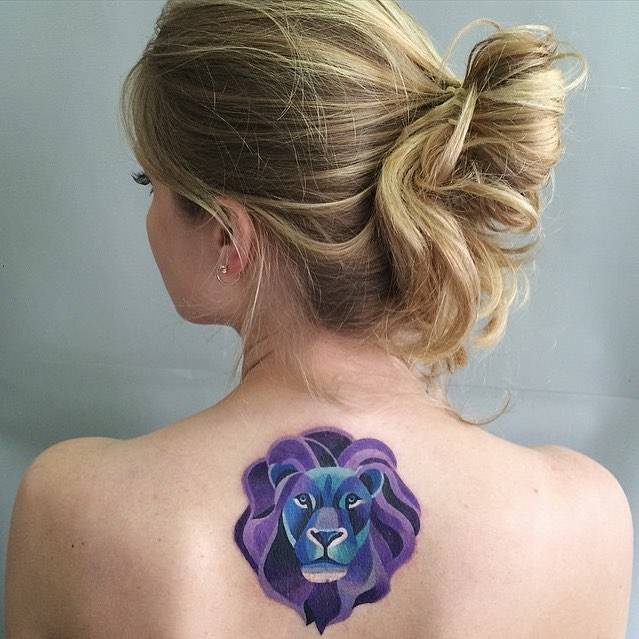 Purple lion head tattoo on the upper back